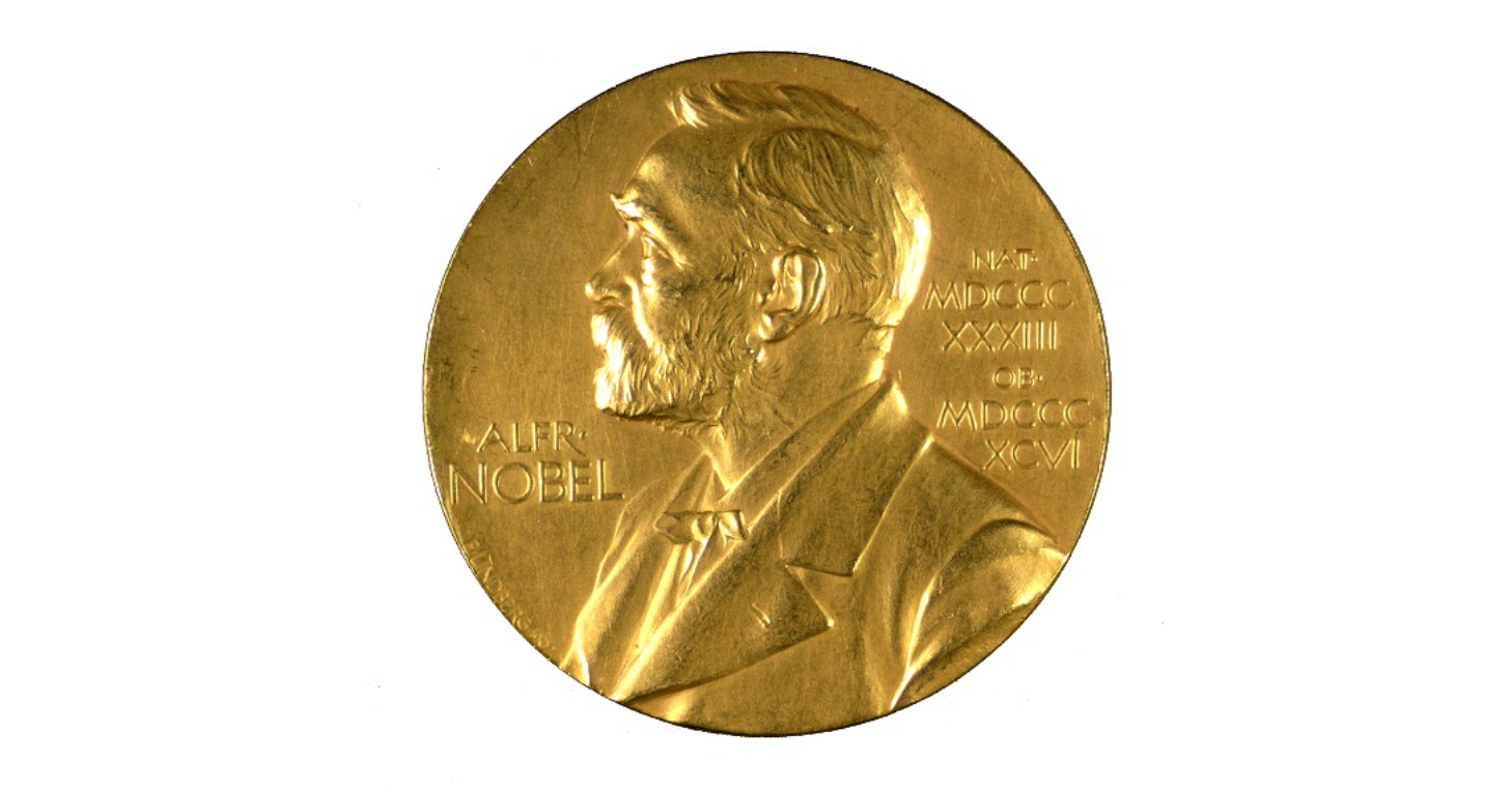 A gold medal with the face of a bearded man in his 60s embossed upon it. The text on the medal reads NOBEL