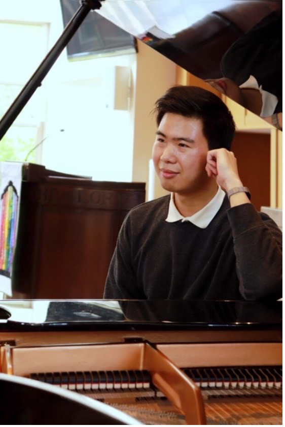 A photo of Di (Steven) Zhai, a male, sitting at a piano in a brown sweater and white collared shirt, looking away from the camera