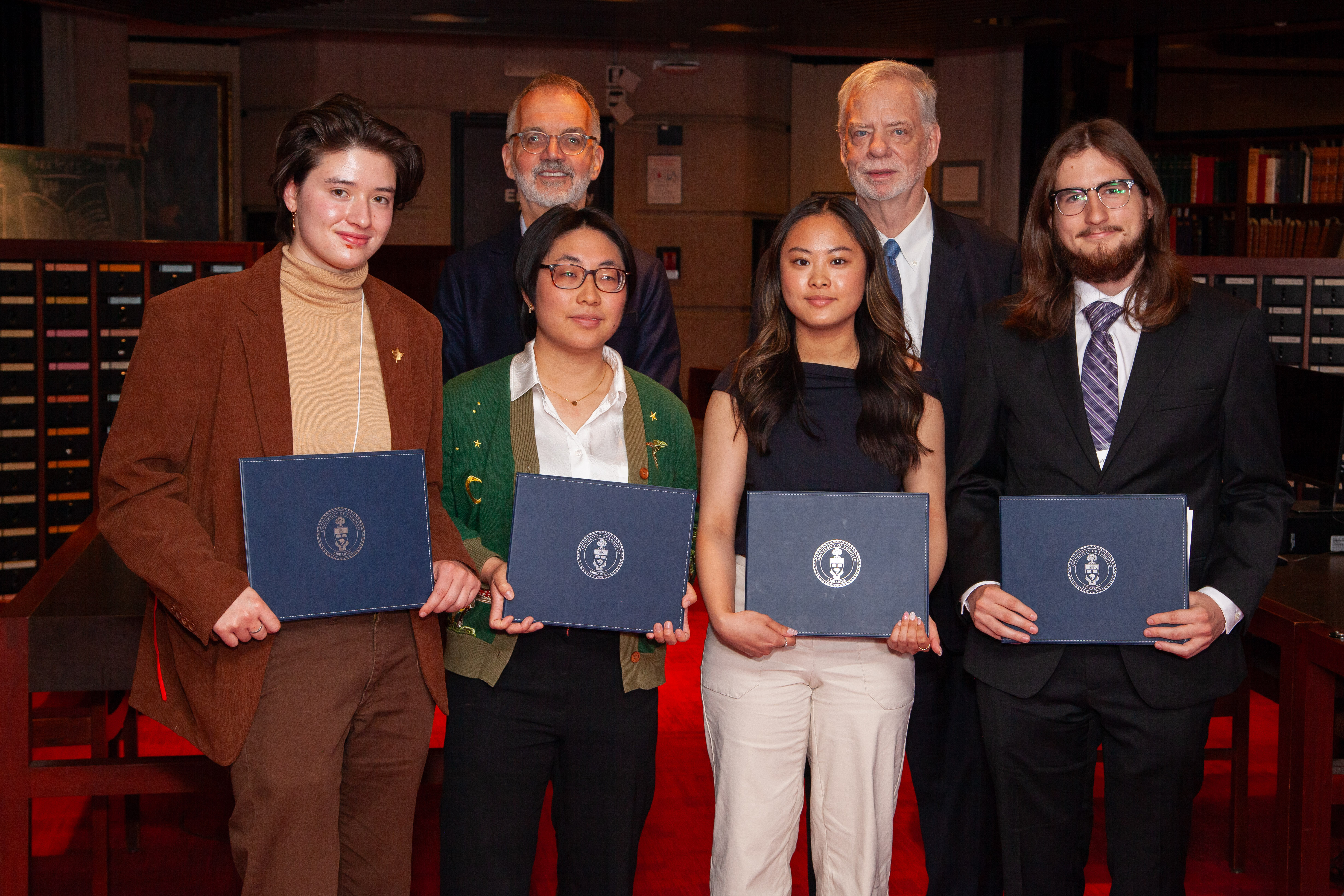 Four students stand in front of two older men with awards.