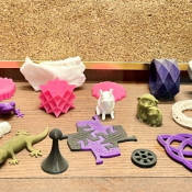 A selection of colourful 3D printed projects is spread across a table.
