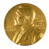 A gold medal featuring the embossed face of a bearded white man in his 60s.