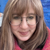 Woman with bangs and glasses standing in front of a blue background