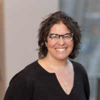 headshot of Mindy Thuna, a white woman with short curly hair and glasses, wearing a black shirt.