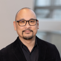 headshot of Glen Morales, a bald man with dark glasses and a goatee, wearing a black shirt and black blazer. 