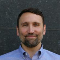 Man with blue shirt, short brown hair, and beard.