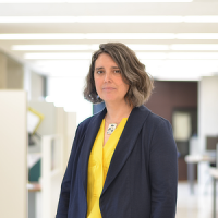 Photo of Kate Davis, a white woman with grey shoulder length hair, a yellow shirt, and navy blazer