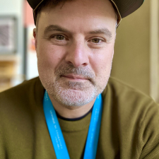 Ben Walsh wearing a dark baseball cap, green sweater, and teal lanyard.