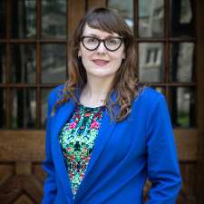 Image of Kate MacDonald wearing blue blazer, coloured dress and glasses.