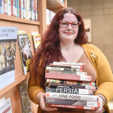 woman with red hair and glasses holding a stack of cookbooks