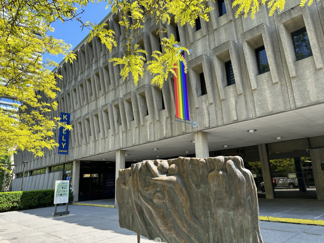 Colour photo of the entrance of the St. Michael's College Library showing sculpture infront of entrance and Pride flag handing over entrance.